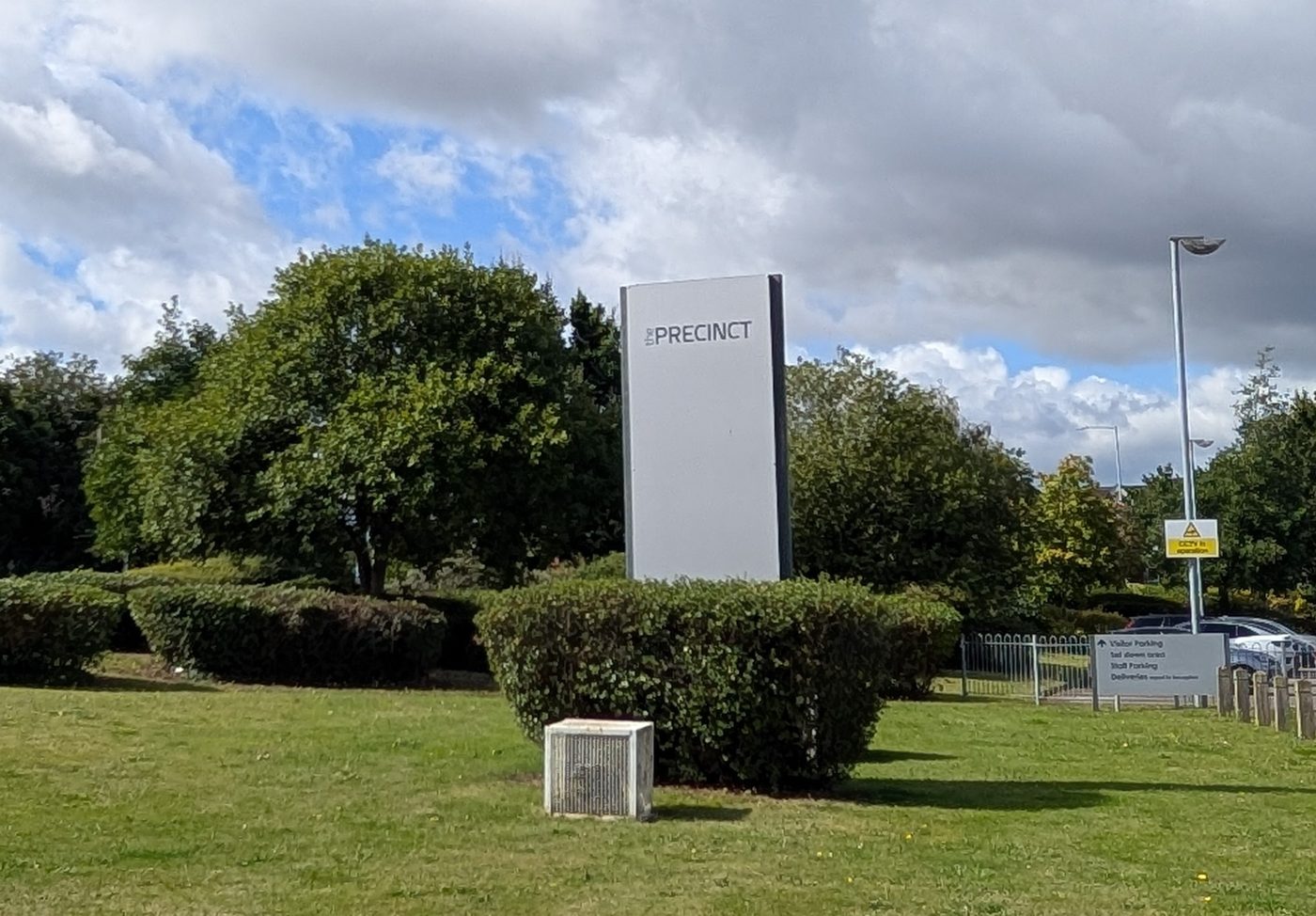 A tall grey monolith sign reading “the PRECINCT” on a landscaped verge at the entrance to UBT's United Kingdom headquarters in Warwick